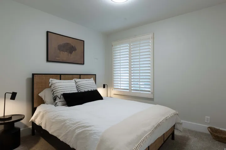 Neutral wall color, window with white plantation shutters, flush-mount ceiling light fixture, and textured carpet flooring