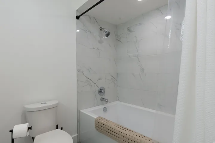 Bathtub and shower combination featuring a tiled surround, recessed lighting, and a black shower rod