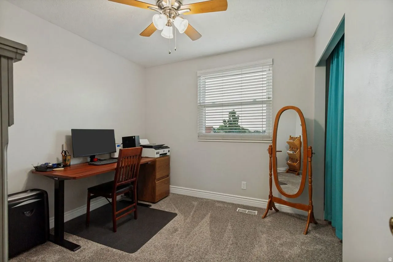 Ceiling fan with light fixture, window with blinds, light gray wall paint, gray carpet flooring, baseboards