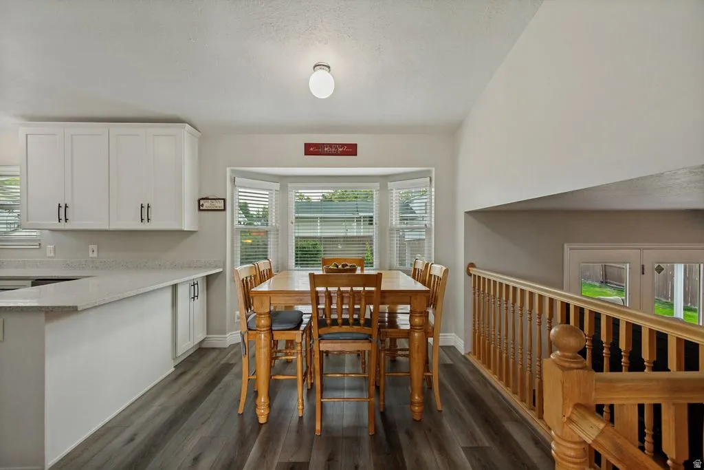 White cabinetry with dark hardware, light countertops, wood-finish flooring, bay window with blinds, and a wood railing