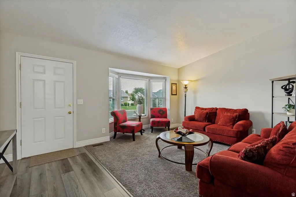 Wood-finish flooring at entry, bay window with blinds, and carpeted living area