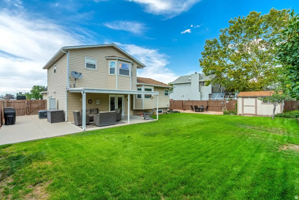 Expansive lawn with a two-story residence featuring siding and a bay window, complemented by a covered patio and a detached storage shed