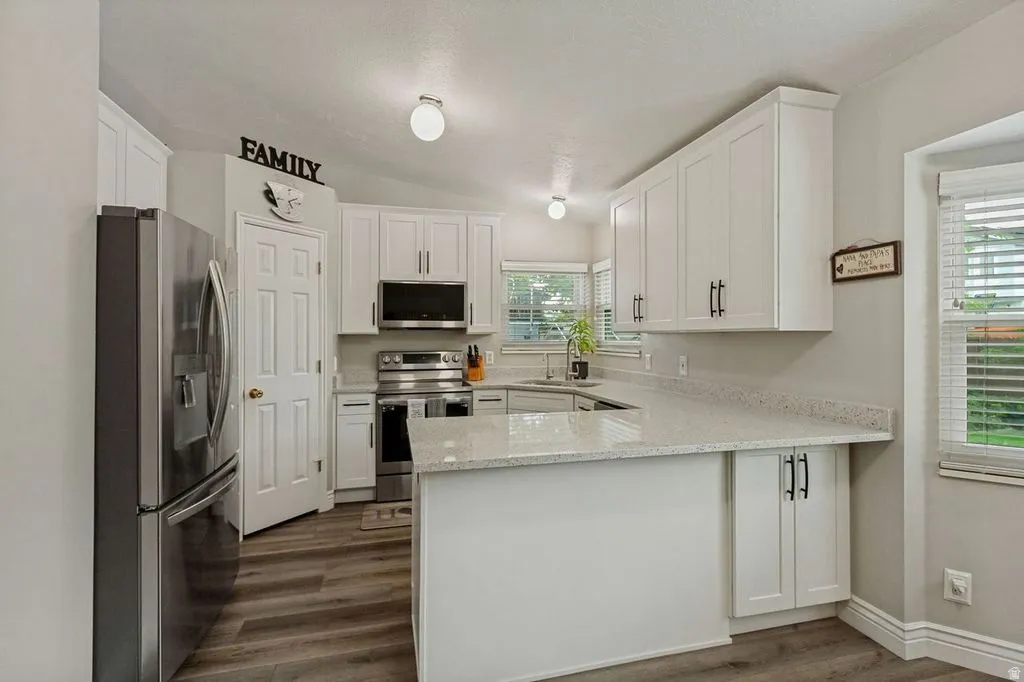 White shaker cabinetry, stainless steel appliances, light-toned countertops, and wood-finish flooring