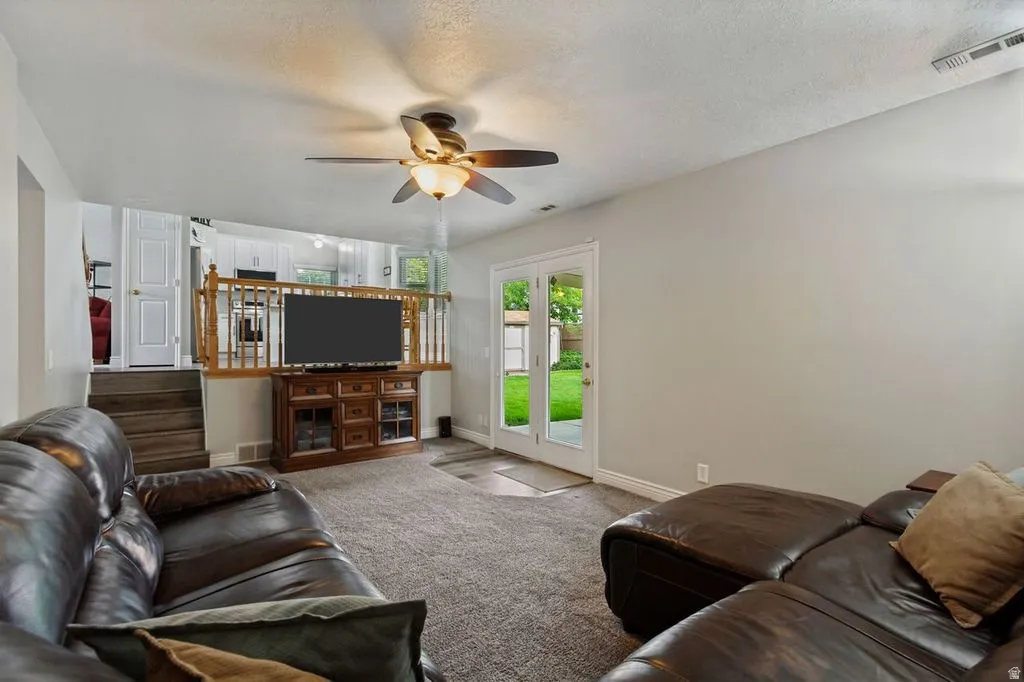 Carpeted living area with a ceiling fan, French doors, and a wood-finish railing