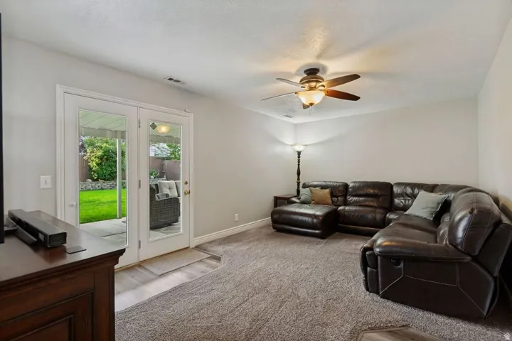 Dual French doors, textured carpeting, overhead ceiling fan with integrated lighting, and light-toned wall finishes