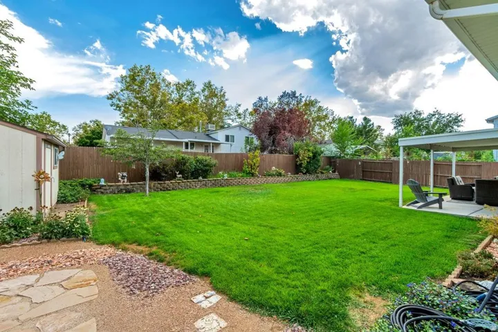 Expansive backyard featuring a lush lawn, privacy fencing, a covered patio area, and a storage shed