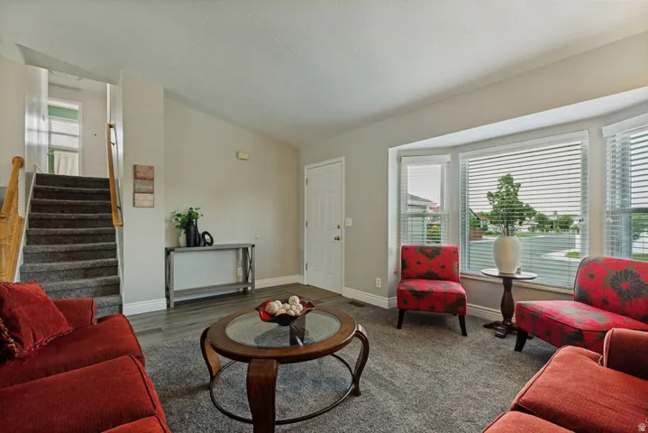 Bay window with horizontal blinds, wood-finish flooring, and carpeted stairs with wood handrail