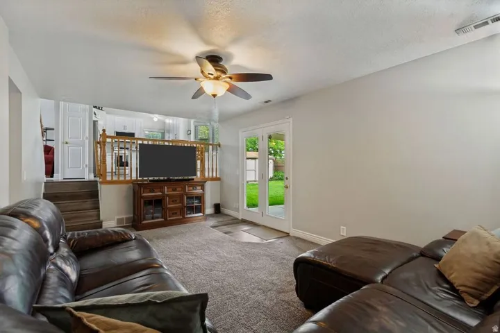 Carpeted living area with a ceiling fan, French doors, and a wood-finish railing