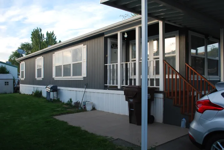 Exterior featuring vertical siding, white window trim and shutters, covered entry porch, and an attached carport