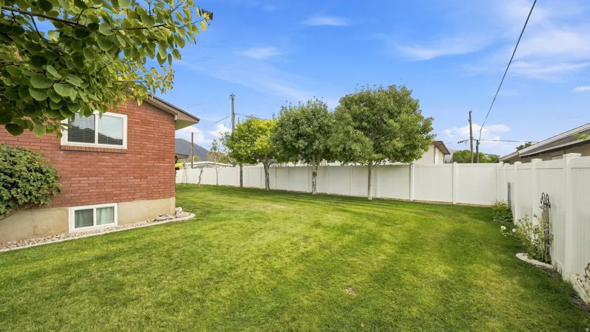 Expansive backyard with lush, manicured lawn bordered by vinyl fencing and mature shade trees