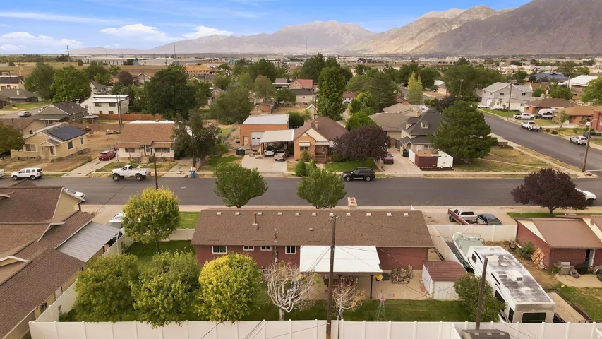 Aerial view showcasing a brick residence with mature landscaping, including established trees throughout the property and grounds