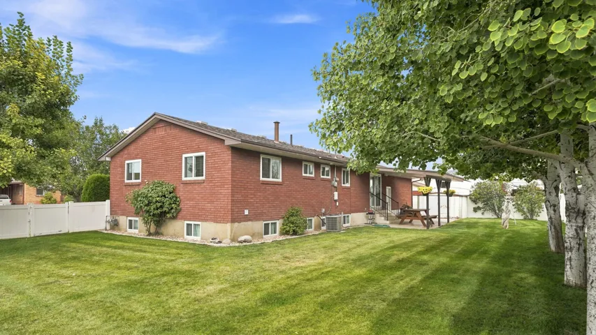 Brick ranch home with multiple windows and a manicured lawn featuring mature shade trees.