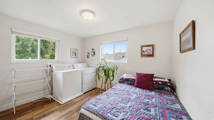 Versatile bedroom with hardwood flooring, large windows providing natural light, and convenient in-room laundry appliances