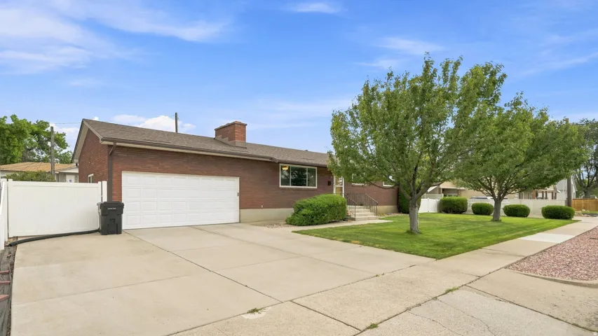 Brick ranch home featuring a two-car garage with white overhead door, expansive concrete driveway, and mature landscaping with established trees and manicured lawn