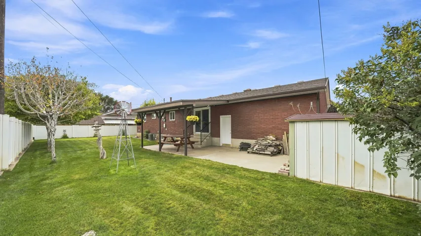 Expansive backyard featuring a mature landscaped lawn with established trees, metal storage sheds, and a brick single-story residence with covered patio area.