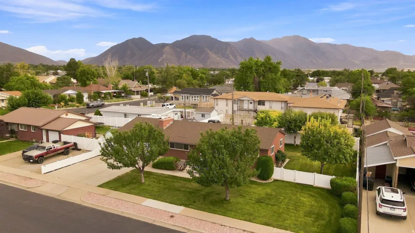 Scenic residential property featuring a brick exterior, manicured lawn with mature landscaping, and mountain backdrop