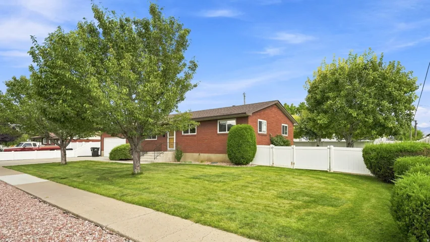 Brick ranch home set on a spacious landscaped lot featuring mature shade trees, manicured lawn, and established hedging