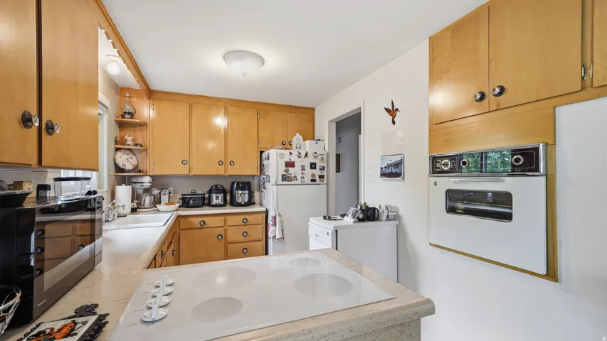 Bright kitchen featuring warm wood-finish cabinetry, including a built-in wall oven, light stone countertops.