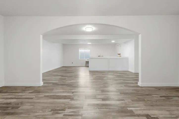 Arched entryway leading to a spacious room with wood-finish flooring