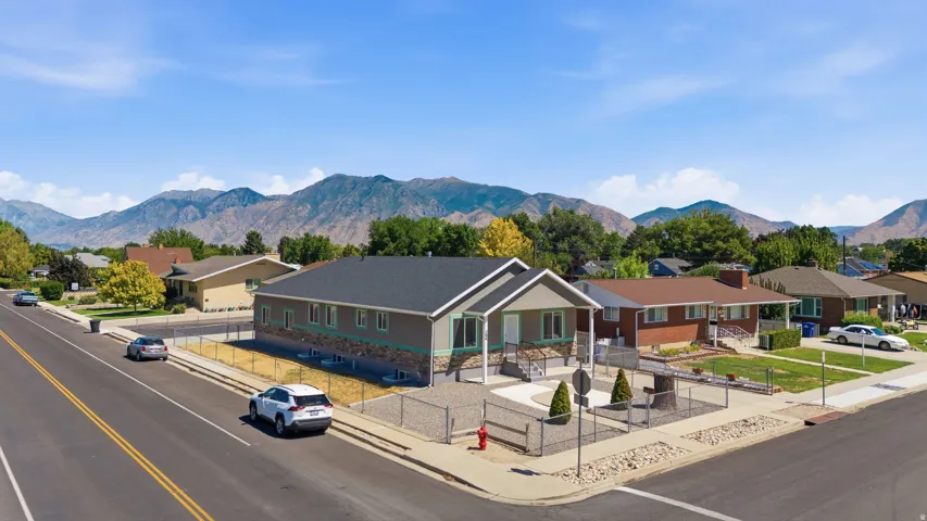 Corner lot property featuring a dark shingle roof, stone veneer accents, and an expansive paved area