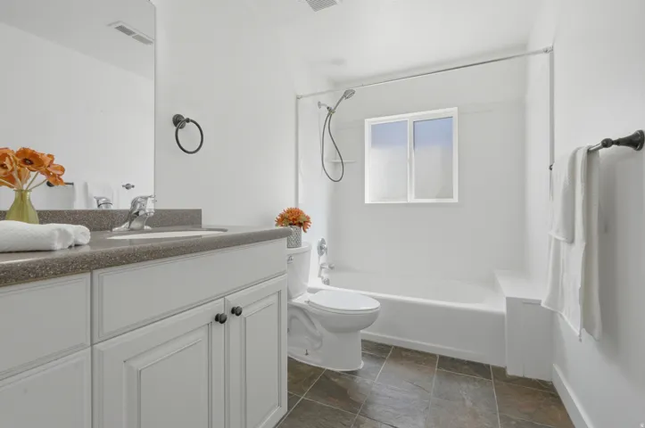 White vanity with dark hardware, integrated sink, and speckled countertop