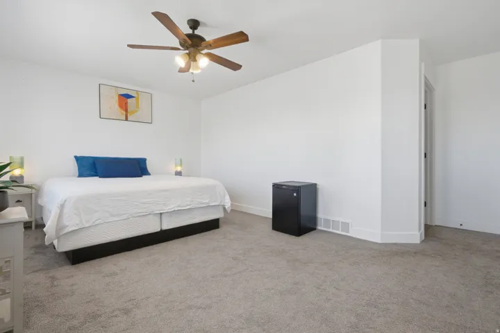 Carpeted flooring, white painted walls, ceiling fan with integrated lighting, and a doorway