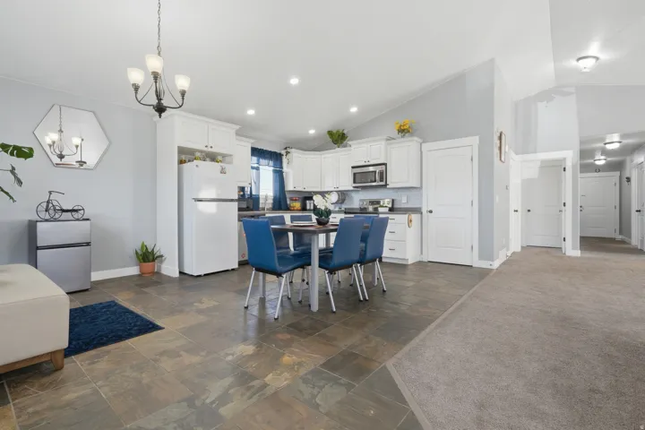 Vaulted ceilings, white kitchen cabinetry, stainless steel microwave, tile flooring, and recessed lighting
