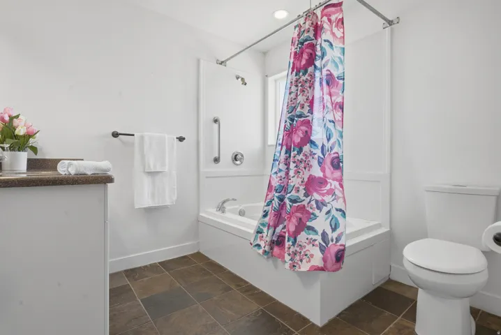 White vanity with a dark countertop, white bathtub with a shower fixture, and dark floor tiles