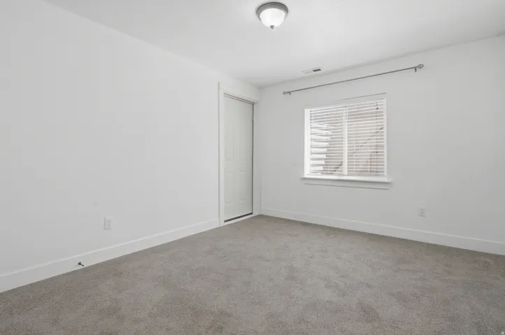 White walls, grey carpeting, and a window with blinds