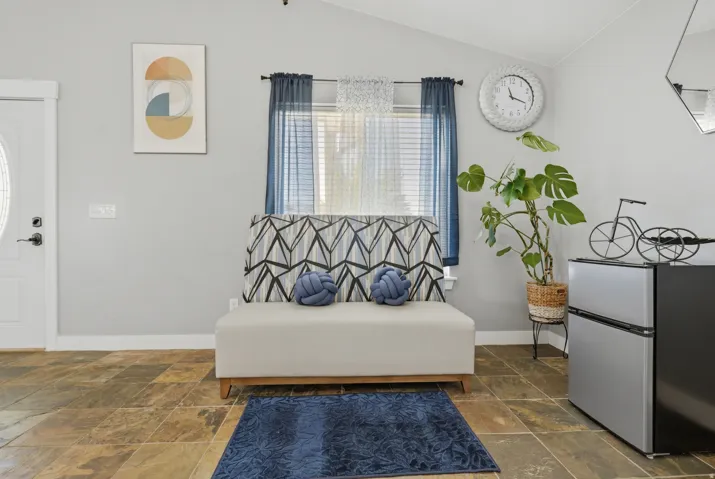 Vaulted ceiling, white paneled door with oval window, window with blinds, gray painted walls, and tile flooring