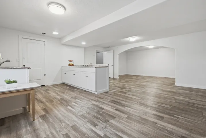 Spacious lower level featuring wood-finish flooring, recessed lighting, white cabinetry, and an arched entry
