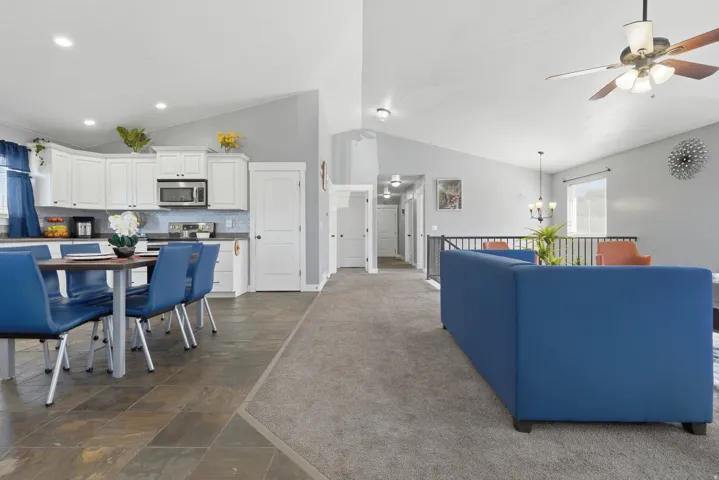 Vaulted ceilings with recessed lighting, white cabinetry with stainless steel appliances, tile backsplash, and a black metal railing