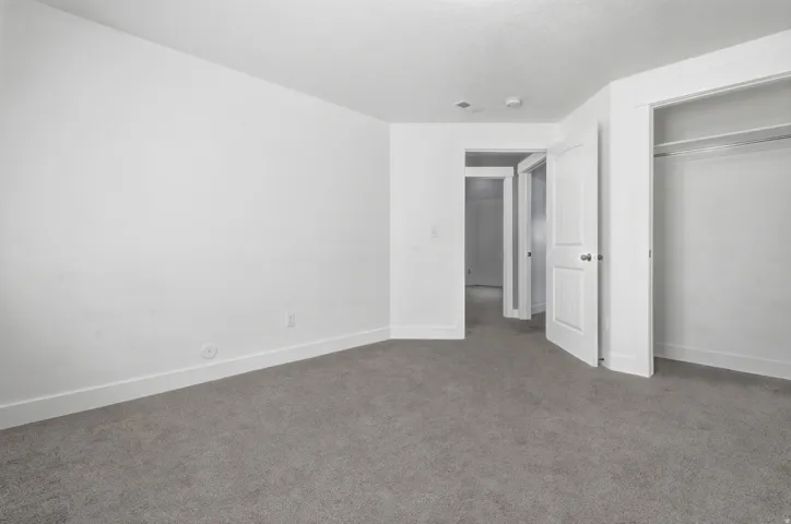 Carpeted flooring, white walls, white trim, solid core doors, and a built-in closet with shelving and hanging rod