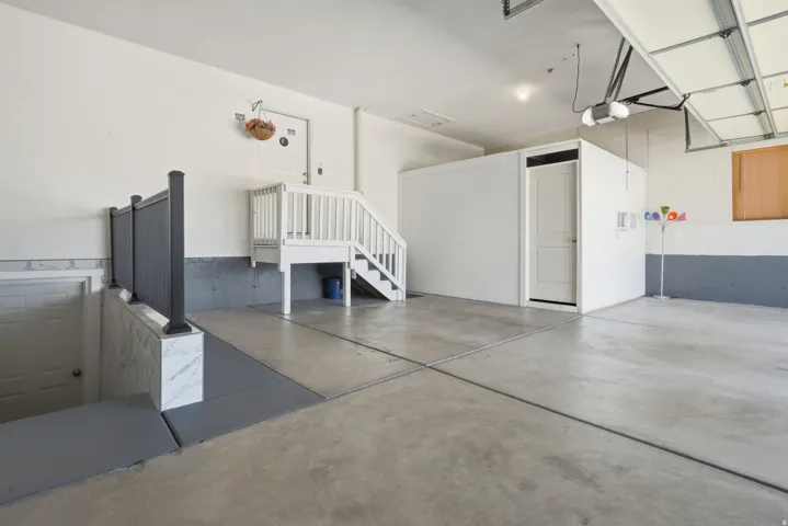 Concrete flooring with expansion joints, white interior walls, built-in storage room, and garage door opener