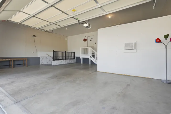 Spacious garage featuring a concrete floor, overhead garage door, interior staircase with white risers and black railings, and an integrated wall-mounted air conditioning unit