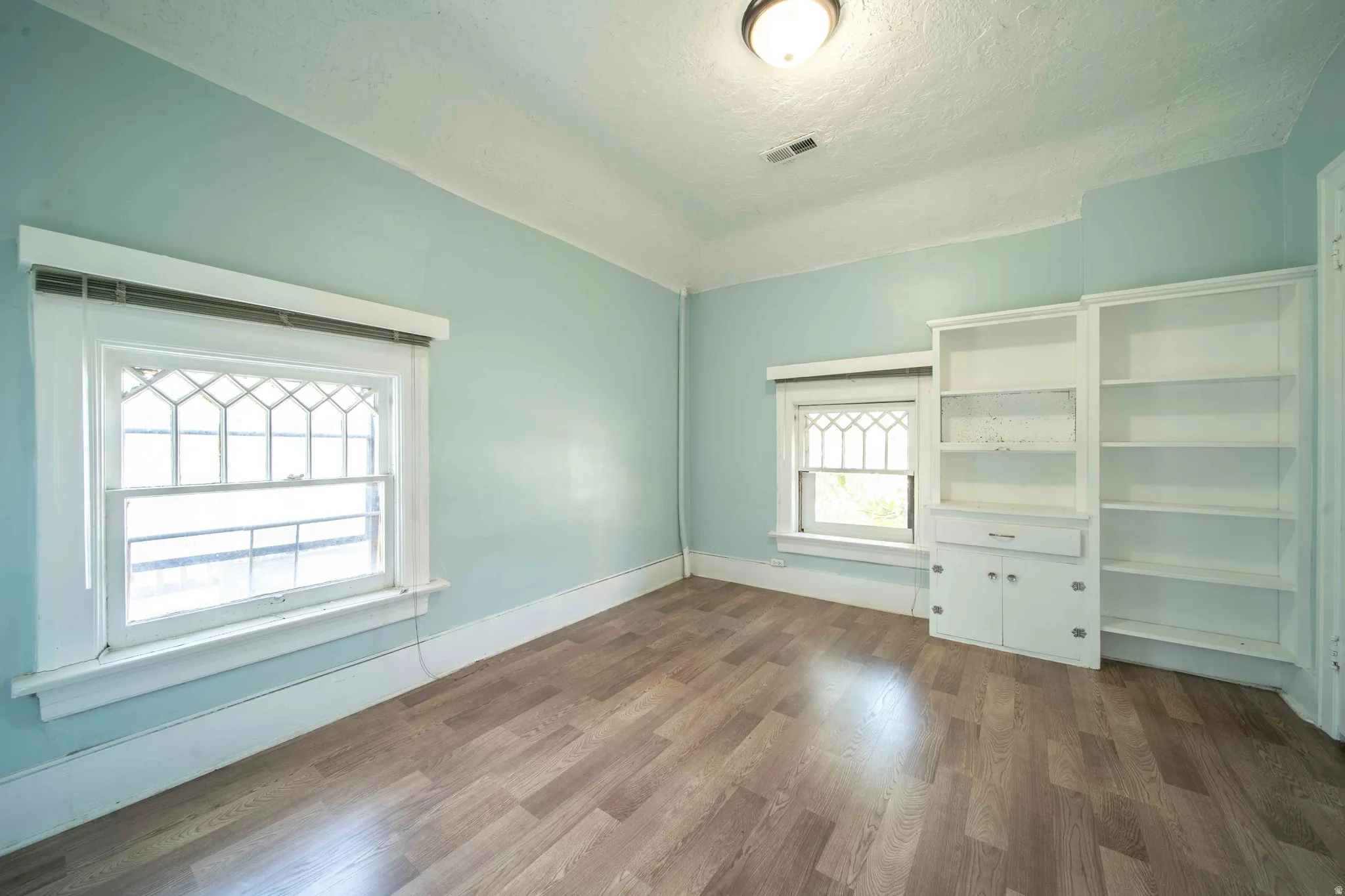 Wood-finish flooring, built-in shelving, built-in cabinetry, and white window trim