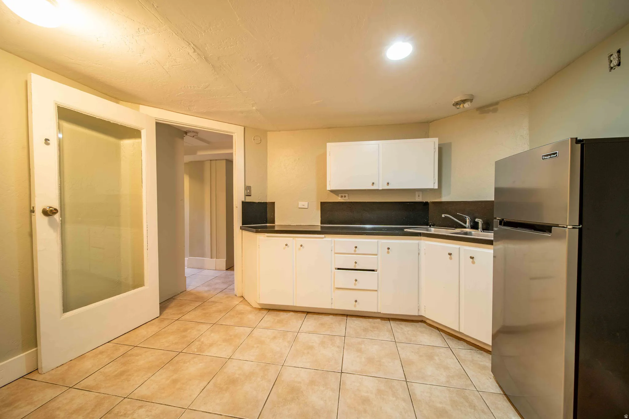 Kitchen featuring white cabinetry, dark countertops, a stainless steel refrigerator, and tiled flooring