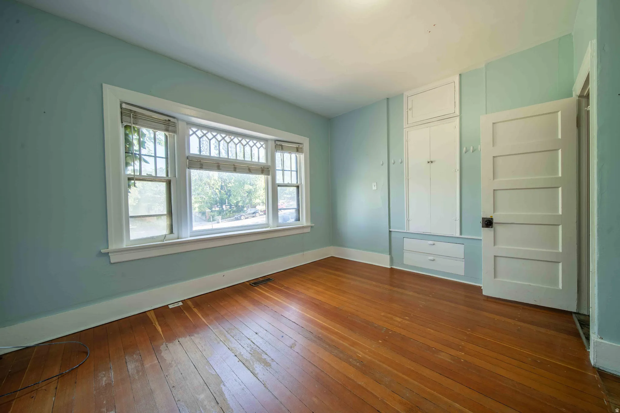 Hardwood flooring, multi-panel door, built-in cabinetry, built-in shelving, and large bay window with decorative muntins