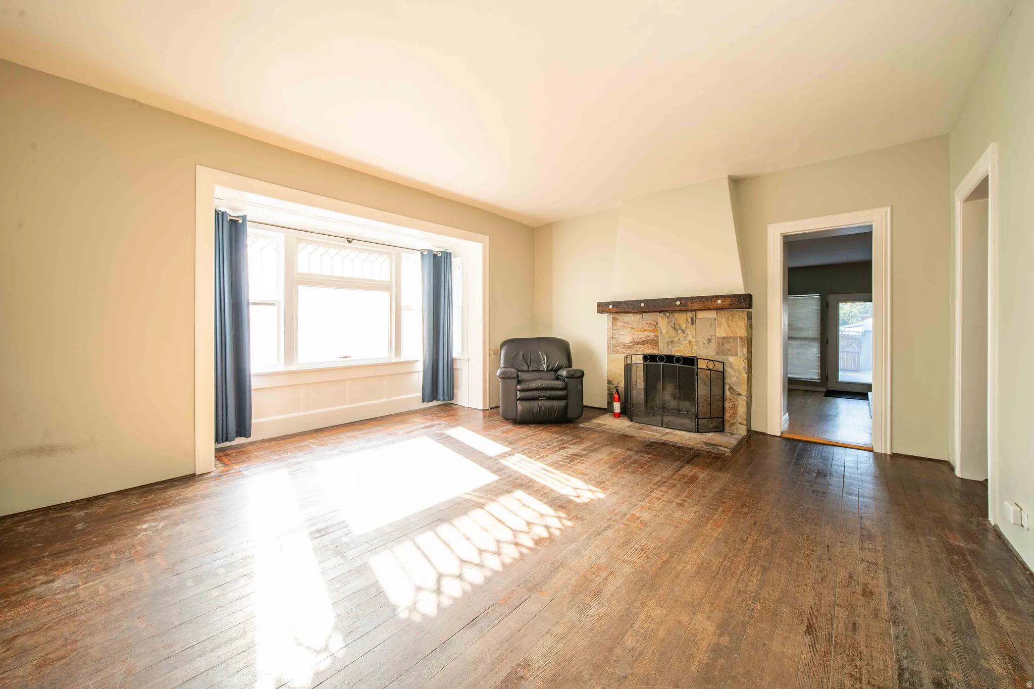 Wood-finish flooring throughout, a stone-clad fireplace with a dark wood mantel, and a bay window
