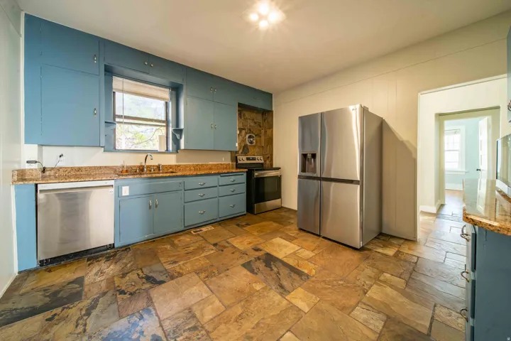 Kitchen featuring slate tile flooring, blue cabinetry, stainless steel appliances, and granite countertops