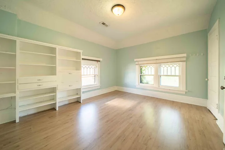 Light wood-finish flooring, built-in shelving, two windows, and a flush mount ceiling light