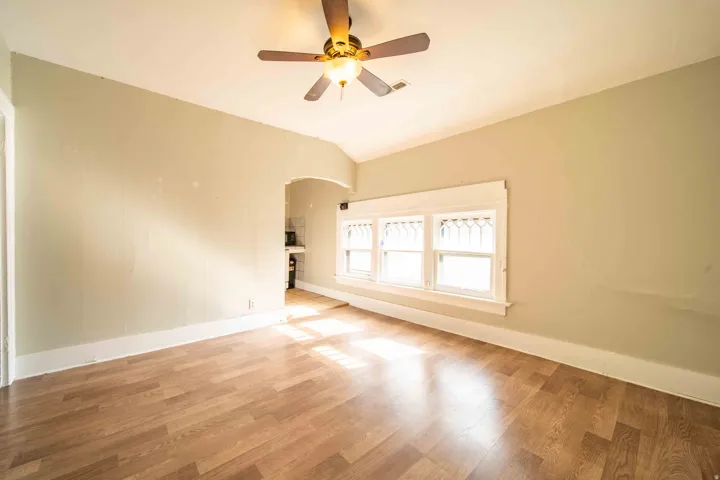 Wood-finish flooring, ceiling fan with integrated lighting, multiple windows with decorative grilles, and an arched doorway