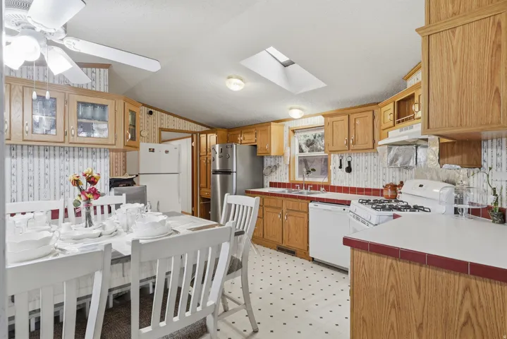 Kitchen featuring wood cabinetry, white appliances, a skylight, and a ceiling fan