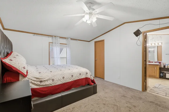 Carpeted flooring, vaulted ceiling, ceiling fan, wood trim, and a paneled door