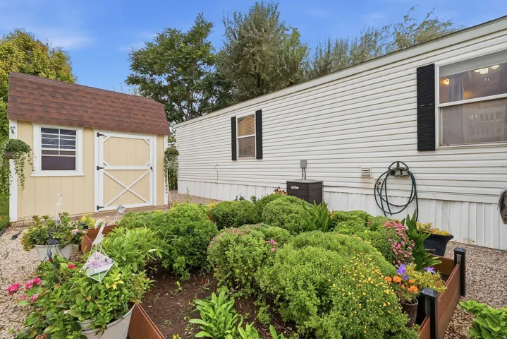 Exterior featuring a garden bed with varied plantings, gravel ground cover, and a storage shed with a shingle roof
