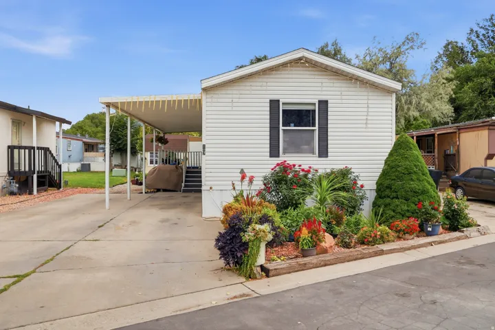 White siding exterior with black shutters, mature landscaping, paved driveway, and covered carport