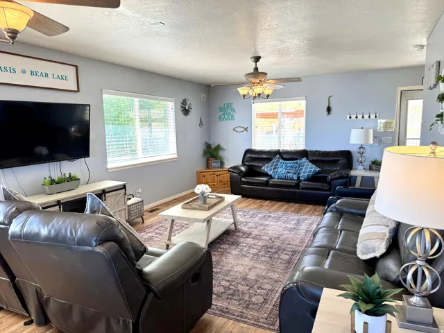 Spacious living area featuring wood-finish flooring, two ceiling fans, and multiple windows with blinds