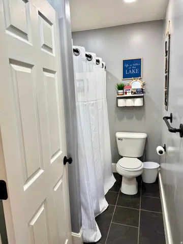 Bathroom featuring dark rectangular floor tiles, a white paneled door with black hardware, and a white toilet