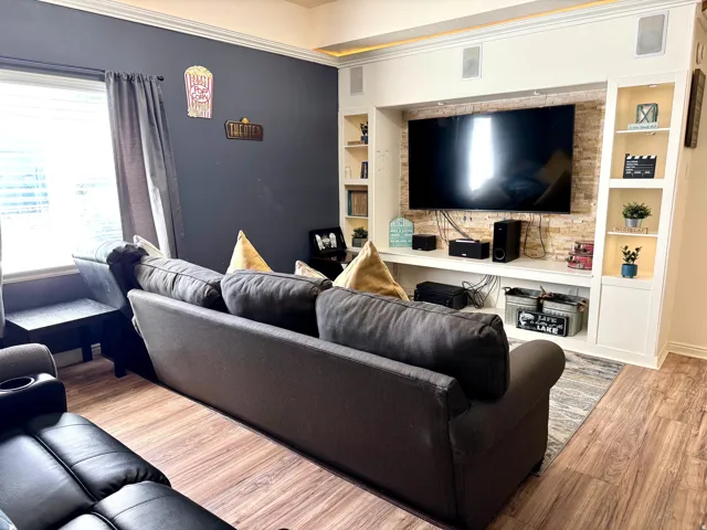 Built-in media center with stacked stone accent wall, integrated shelving, crown molding, and wood-finish flooring