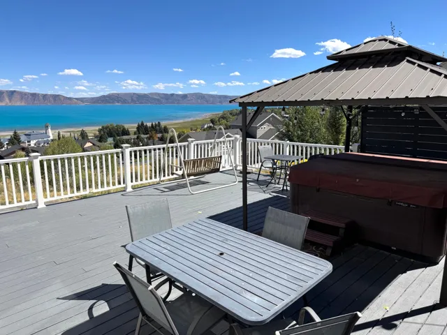 Expansive deck with lake and mountain scenery, featuring a hot tub, a built-in gazebo, and white railing